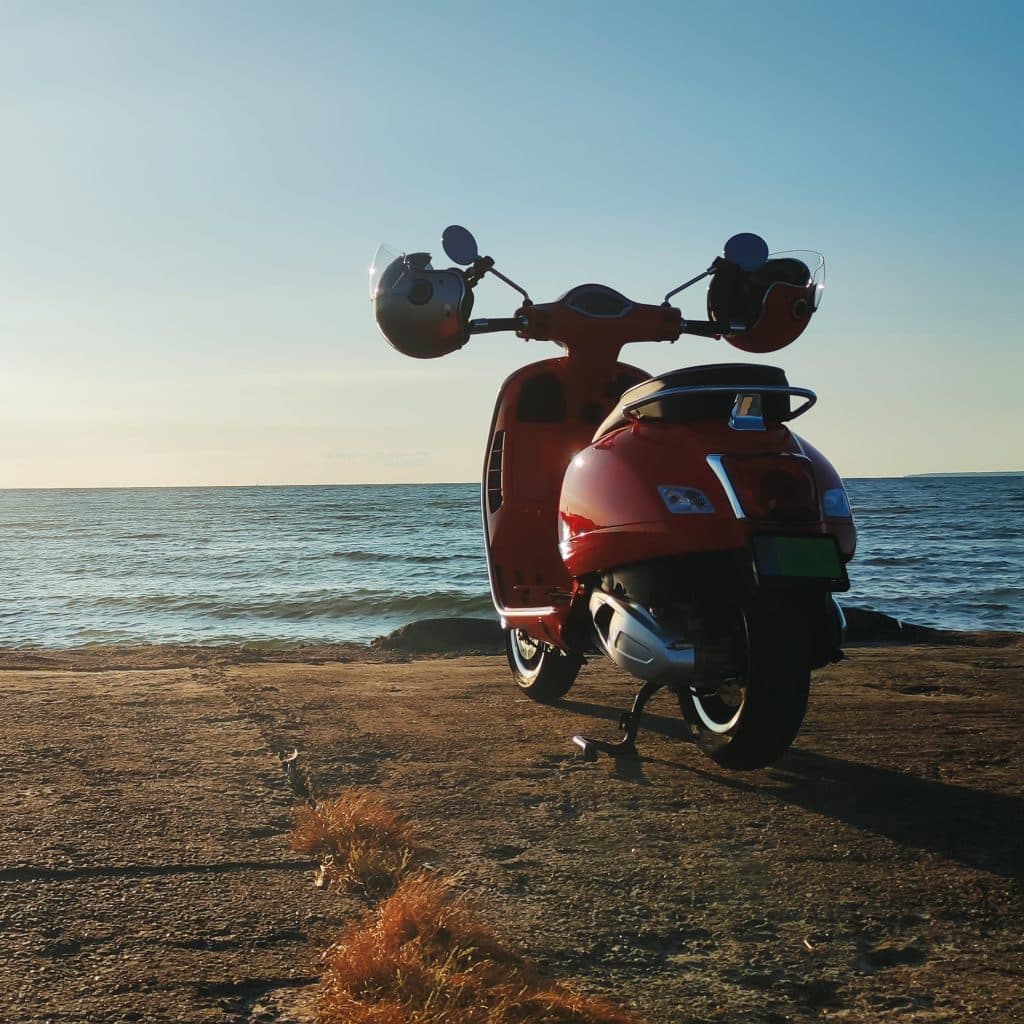 Vespa rossa parcheggiata sulla spiaggia di Stintino al tramonto, mare turchese sullo sfondo